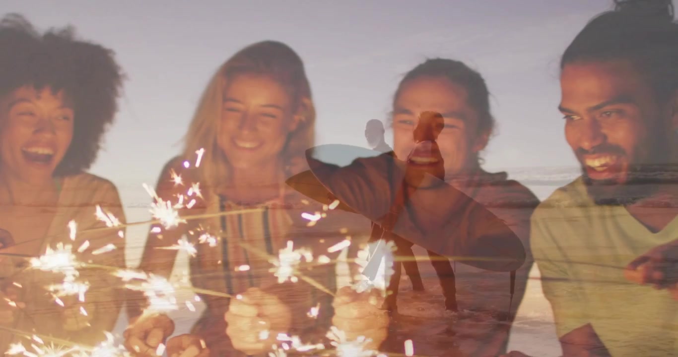 Vertikales Video: Wunderkerzen werden angezündet, fünf Personen reichen sie an einem Strand in der Dämmerung weiter, ein Paar geht mit Boards.