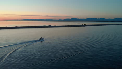 an aerial view following a boat as it turns away from the setting sun