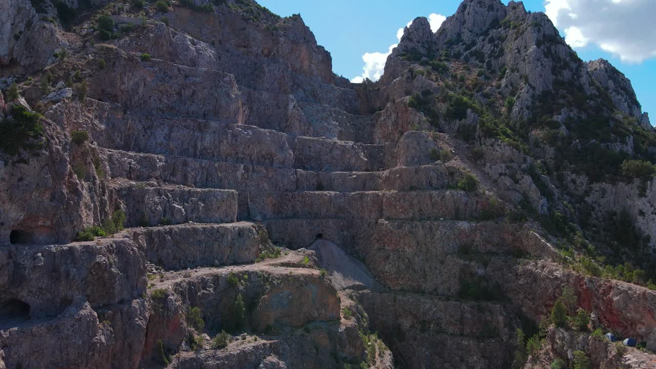 A dramatic view of a winding pathway carved through rugged, layered rock formations in the scenic Jbal Ressas canyon, showcasing nature's raw beauty and geological wonder.