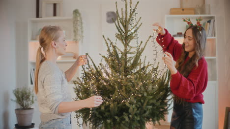 Amigas-Decorando-El-árbol-De-Navidad-Con-Luces