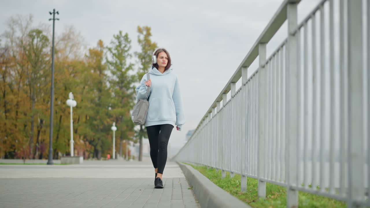 Female music artist wearing sweater and headphones, walking boldly with ...