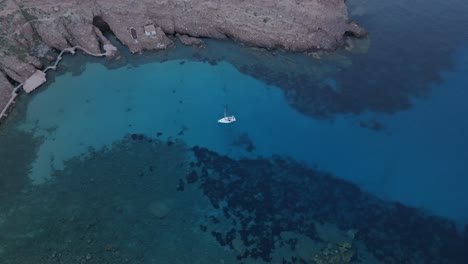 el avión no tripulado desciende en un velero anclado en la bahía rocosa azul profunda en españa.
