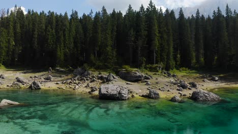 Side-shot-of-Lake-Carezza's-show-with-rocks,-trees-and-mountains-in-the-background