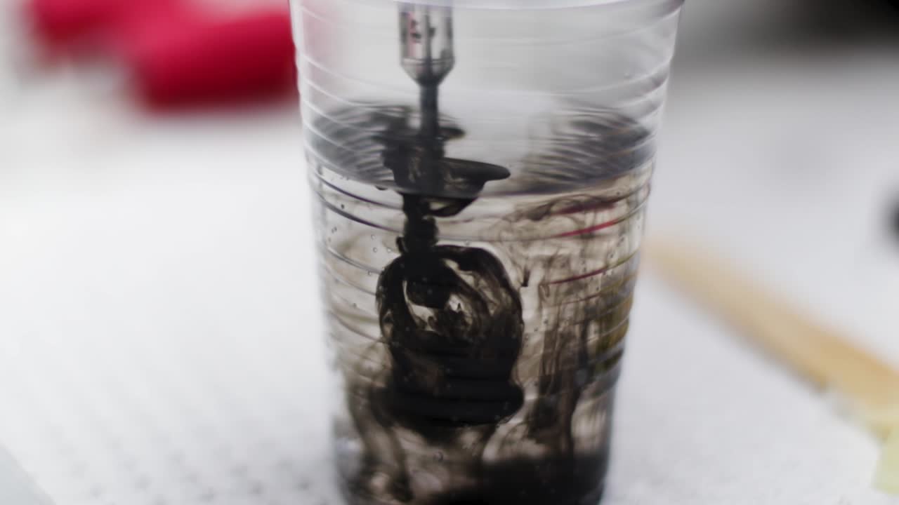 잉크 색상을 변경하기 위해 물에 바늘을 청소하는 문신 예술가