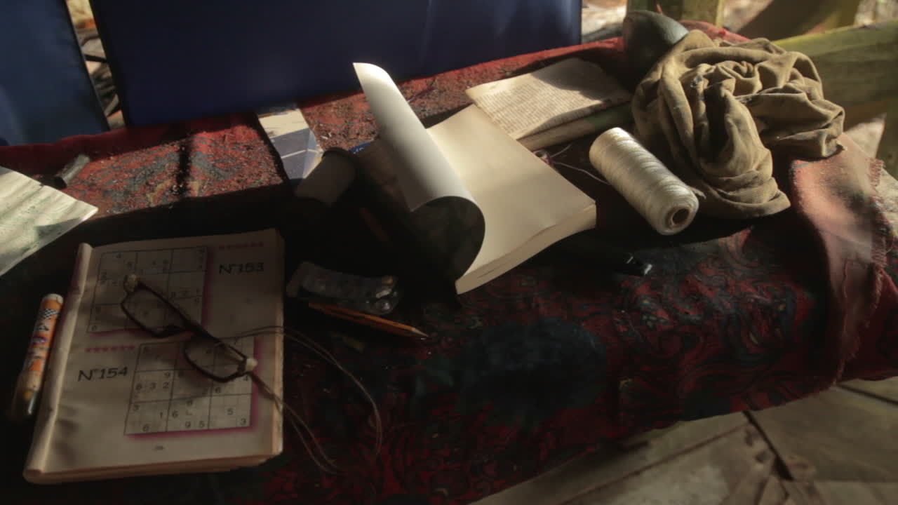 A still life of solitude: a sudoku magazine, thick glasses, and a book rest on weathered rustic desk.