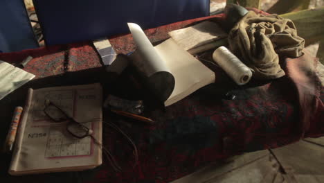 a still life of solitude: a sudoku magazine, thick glasses, and a book rest on weathered rustic desk.