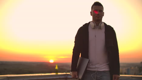 a man walks on the roof in a hoodie with a laptop in his hands to meet the camera.