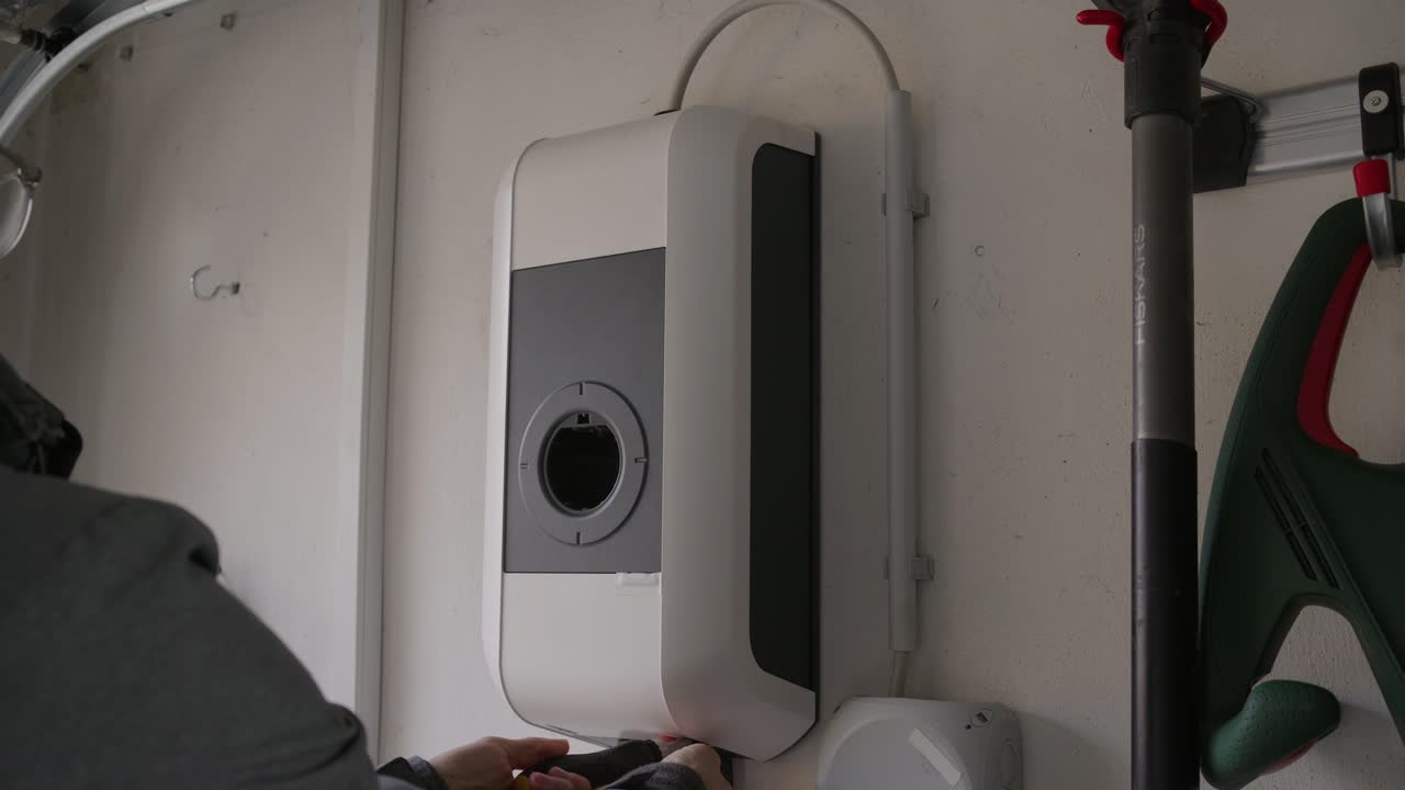 Wide shot of an EV charging station mounted on a wall. The technician opens the large protective cover to access the internal electrical components and configuration ports