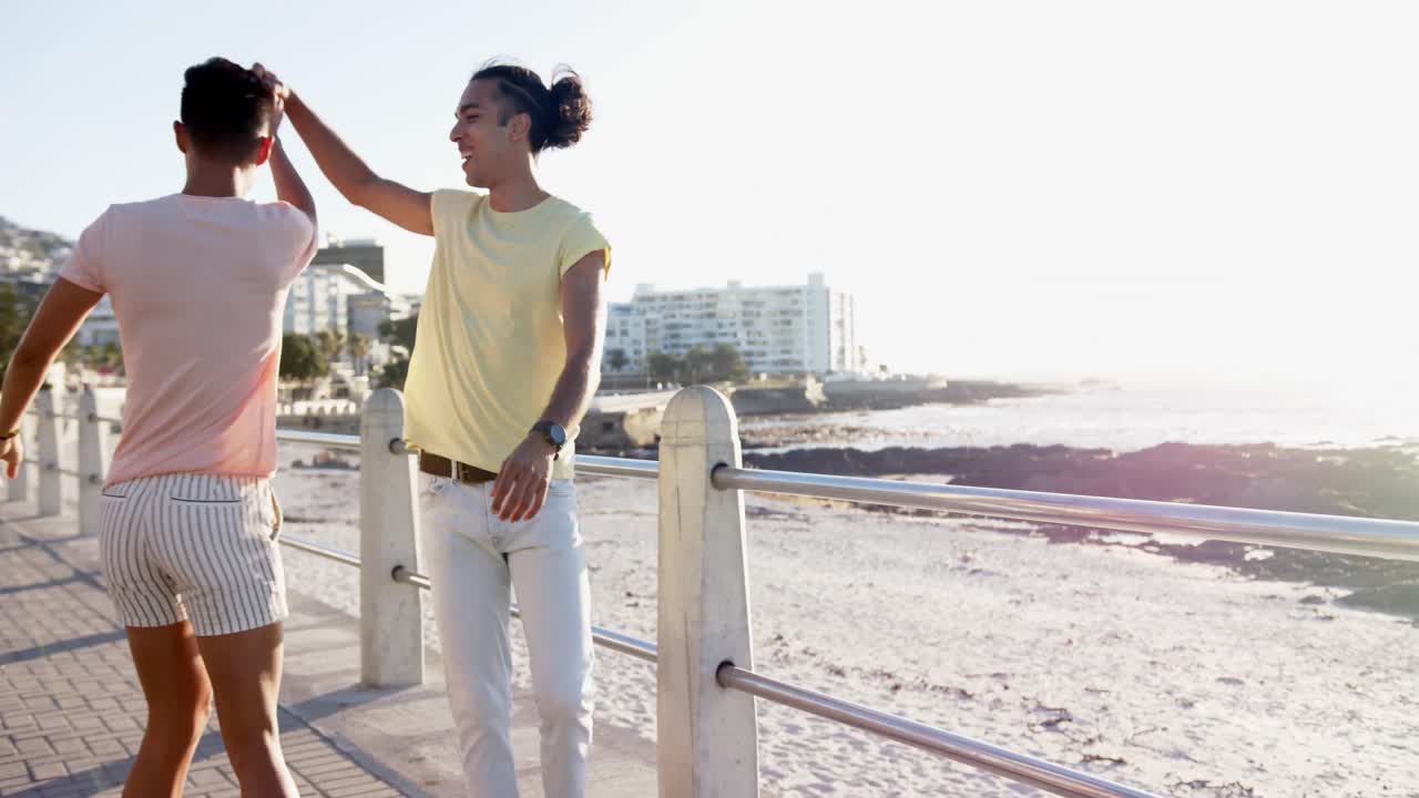 Happy diverse gay male couple dancing at promenade by the sea, slow motion