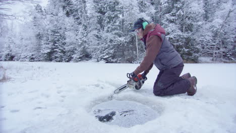 woman with chainsaw starts cutting an ice hole for ice bathing in frozen lake