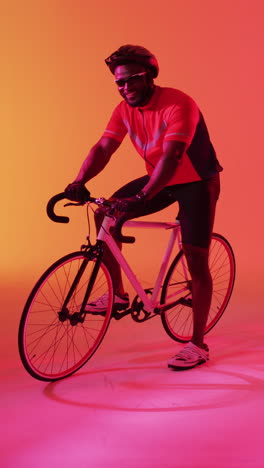 vertical video of happy african american male cyclist looking at camera on orange background