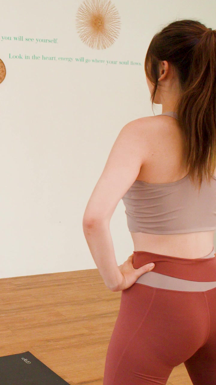 A fit woman in activewear stands confidently in a bright wellness studio with natural lighting.