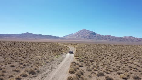 black convertible car driving down a dirt road in the nevada plains fading off into the distance