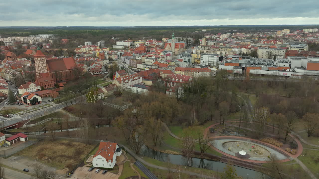 una vista aérea del centro histórico de la ciudad de olsztyn, polonia, con sus coloridos edificios, prominentes techos rojos y el castillo, todo entrelazado con los espacios verdes de la ciudad y un río sinuoso