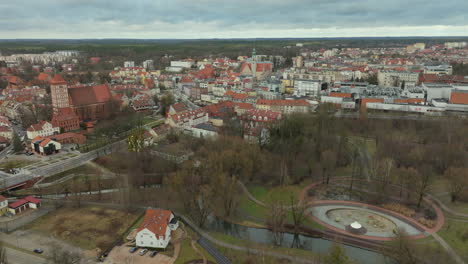 Una-Vista-Aérea-Del-Centro-Histórico-De-La-Ciudad-De-Olsztyn,-Polonia,-Con-Sus-Coloridos-Edificios,-Prominentes-Tejados-Rojos-Y-El-Castillo,-Todo-Entrelazado-Con-Los-Espacios-Verdes-Del-Parque-De-La-Ciudad-Y-Un-Río-Sinuoso