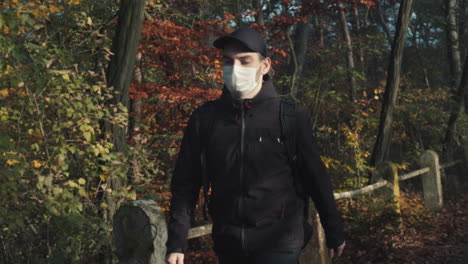 tourist man wearing face mask and walking along forest, life after covid pandemic, middle front view shot