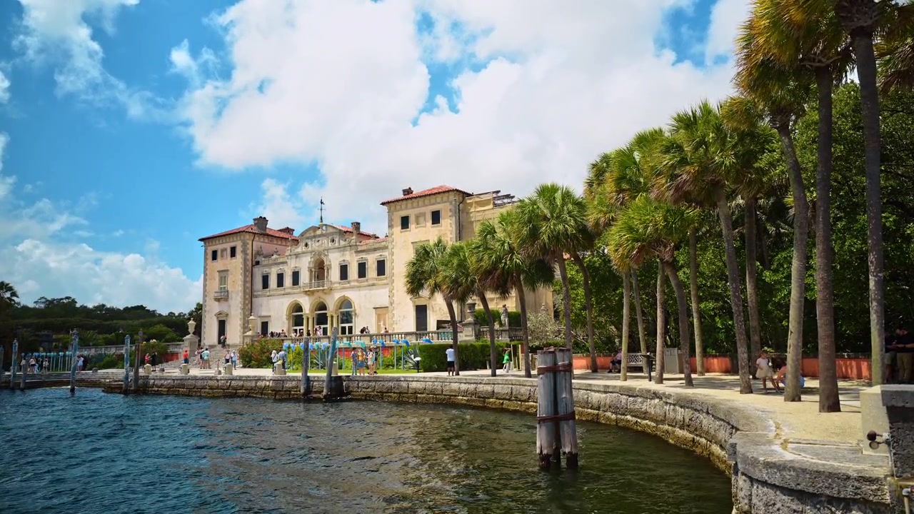 Miami, USA, 16 aprile 2026: Museo Vizcaya visto dalla baia con la passeggiata fiancheggiata da palme, Miami, Florida. Visitatori che camminano lungo il molo vicino a una villa in pietra con giardino e tetto in terracotta.