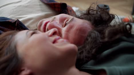 Close-up,-a-happy-brunette-guy-with-curly-hair-lies-on-the-floor-head-to-head-with-his-brunette-girlfriend-and-talks-and-laughs-at-home-in-a-modern-apartment