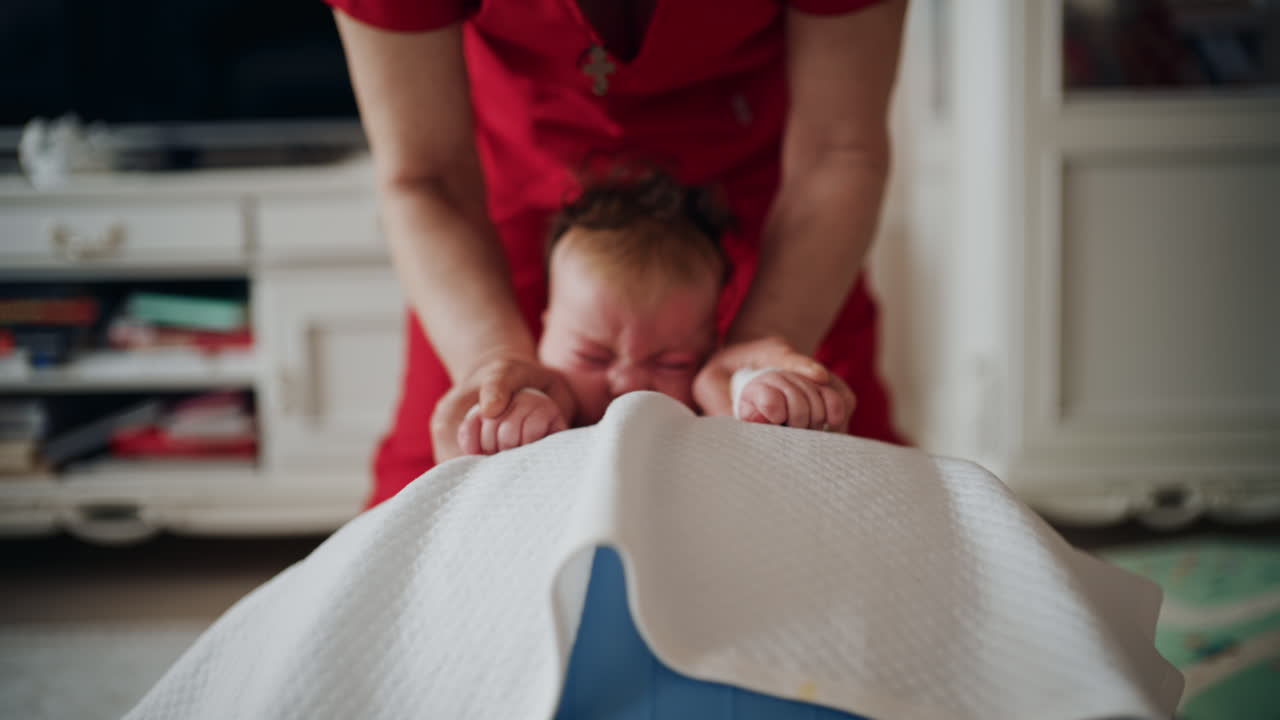 Baby placed on tummy on a stability ball while adults support the infant's torso and shoulders
