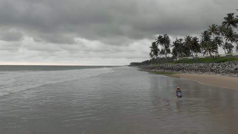 toma aérea de 4.000 drones de una hermosa niña india de 27 años disfrutando de su tranquilo paseo por la playa con el fondo cubierto por nubes lluviosas a lo largo de la costa de varkala