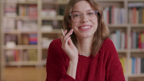 Süßer-Kaukasischer-Student-Mit-Brille-In-Der-Bibliothek,-Der-In-Die-Kamera-Lächelt