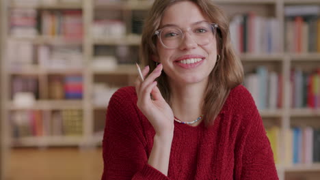 lindo estudiante caucásico con gafas en la biblioteca sonriendo a la cámara