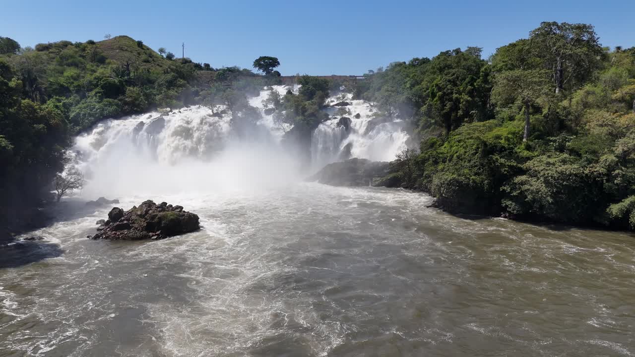 Low-altitude aerial footage of Binga Falls, Angola, showing the lower cascades and fast river currents blending with sunlight and tropical greenery