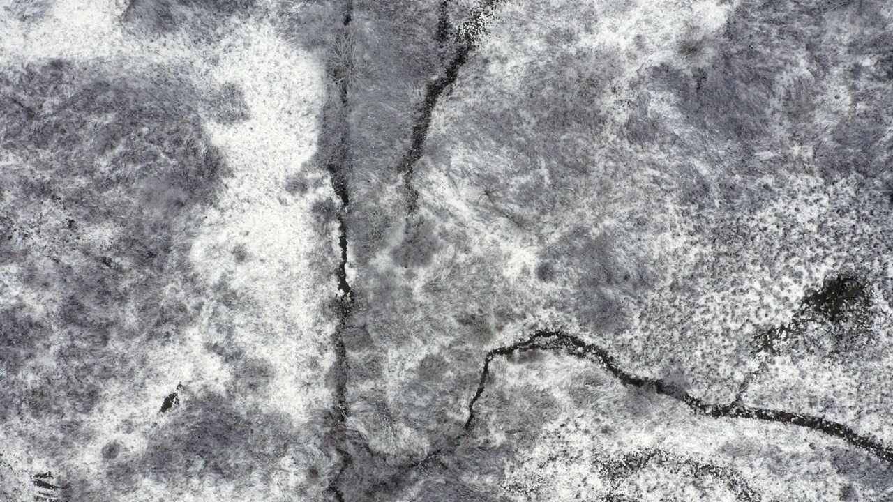 Drone topshot of snow covered hills with cold streams flowing down them.