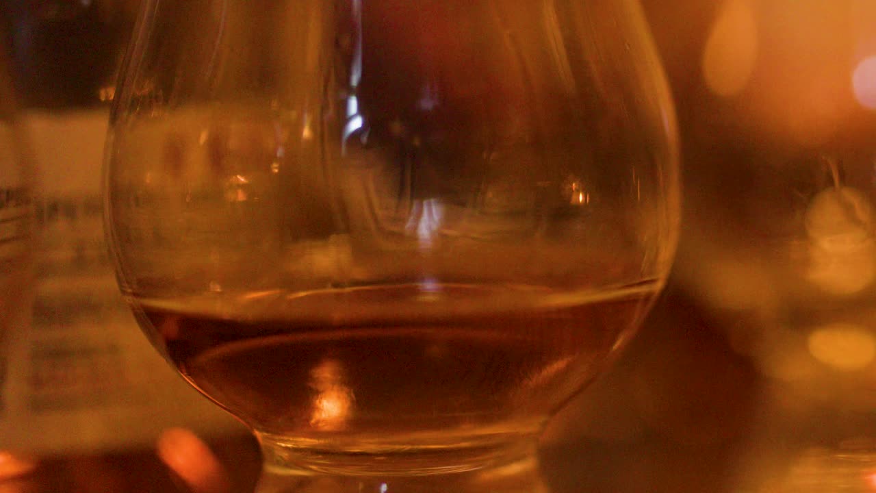 Close-up of whisky glass swirling, amber liquid reflecting warm evening bar lighting, shallow focus