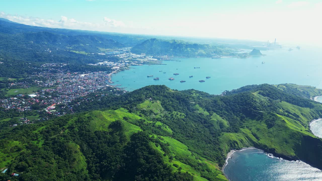 Pull‑out high aerial of Mariveles town in Bataan, seen from Nagbayog View Deck, revealing the coastal settlement, harbor, and surrounding lush green hills against the sea horizon