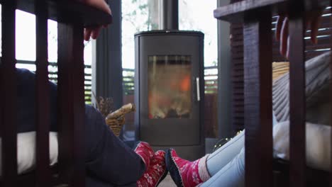 vista trasera de una pareja cogida de las manos mientras está sentada cerca de la chimenea en la casa de vacaciones