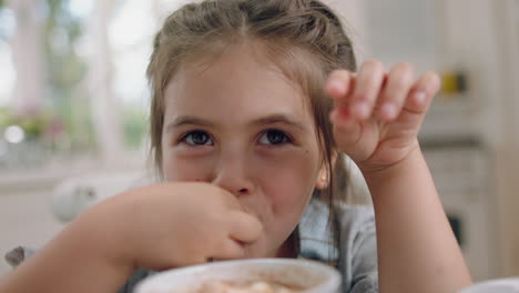 cute little girl eating cookie dipping biscuit into hot chocolate enjoying delicious treat at home in kitchen