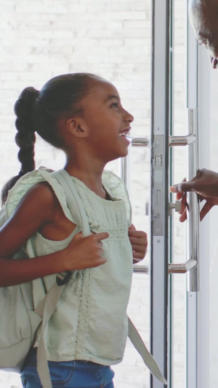 Vertical video: Entering child adjusting backpack straps in green top at home, parent guiding