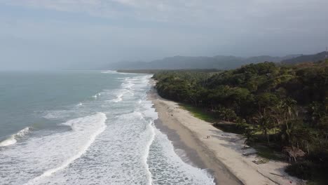 Tourist-couple-walks-empty-sand-beach-on-Caribbean-Sea-by-lush-jungle