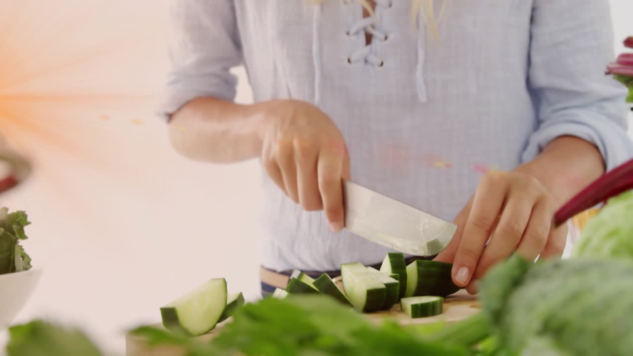 Home cook grabbing chef's knife slicing cucumber for salad while green lens flare sweeping frame