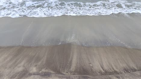 slow motion view of beach waves curling upon a black sandy beach