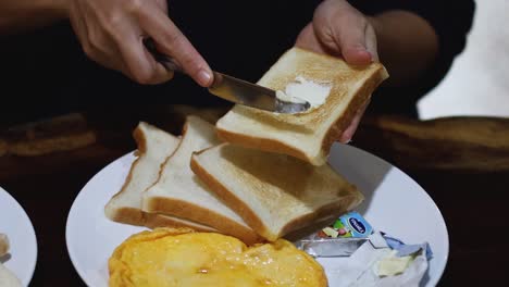 spreading butter on toast beside a plate of omelette