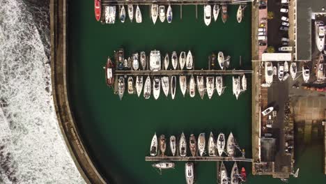 Aerial-top-down-eye’s-bird-drone-view-over-rows-of-boats-moored-at-harbor-with-ocean-waves