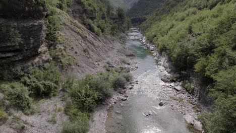 Drone-video-of-ascending-frontal-plane-advancing-over-the-interior-of-the-Cemi-river-on-the-Sh20-road-between-the-mountains-in-Albania-between-Tamarë-and-Selcë,-cloudy-sky-and-turquoise-river-waters