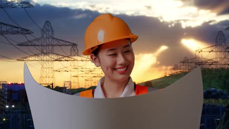 close up de ingeniera asiática con casco de seguridad mirando el plano en sus manos y mirando a su alrededor mientras está de pie cerca de la torre de alto voltaje
