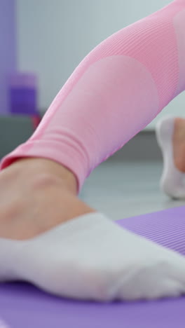 보라색 운동 매트에서 피트니스 훈련 세션 중에 다리의 클로즈업, 개인은 배경에서 빛이 비치는 동안 스트레칭과 운동 움직임을 수행하고 있습니다.
