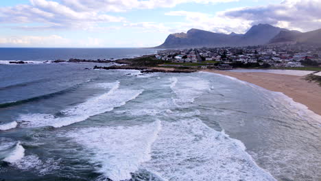 drone pullback view over kleinmond scenic blue flag beach as waves run out