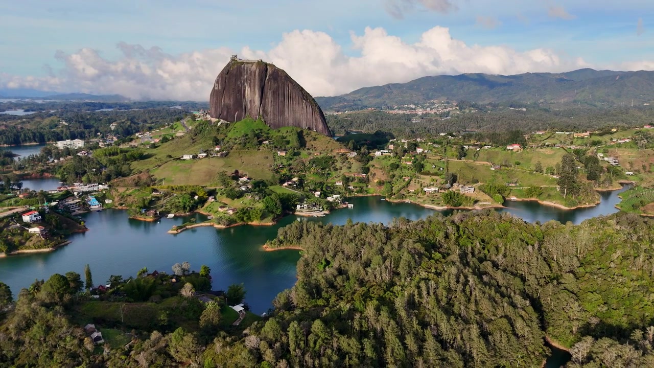 Una ripresa orbitale cinematografica con drone che mostra l'iconica Piedra del Peñol circondata da laghi turchesi e lussureggianti montagne andine verdi a Guatapé, Antioquia, Colombia.