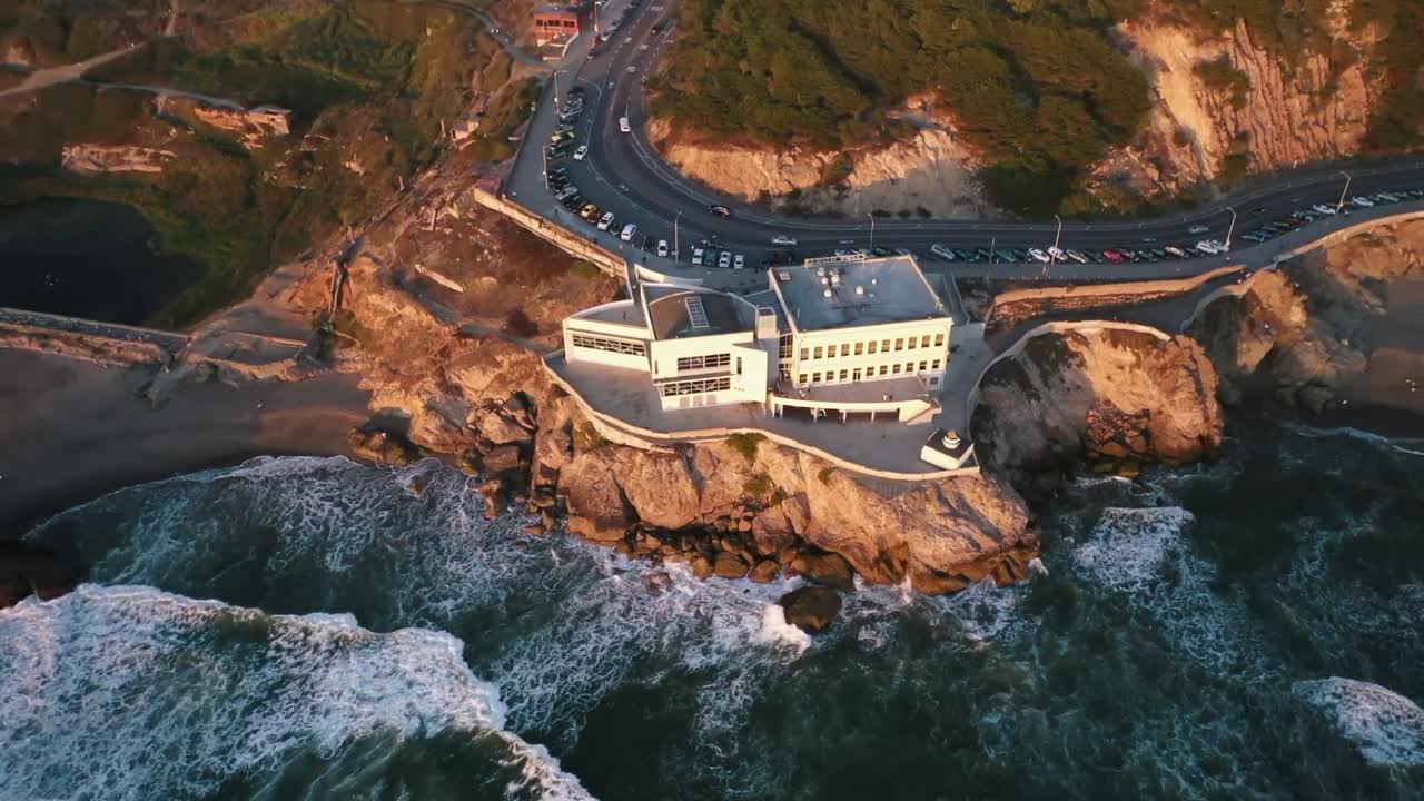 Aerial drone view showing Laaloa Bay Magic Sands Beach with turquoise water, rocky coast, palm trees, and seaside buildings under warm sunlight in Kailua Kona on Big Island Hawaii