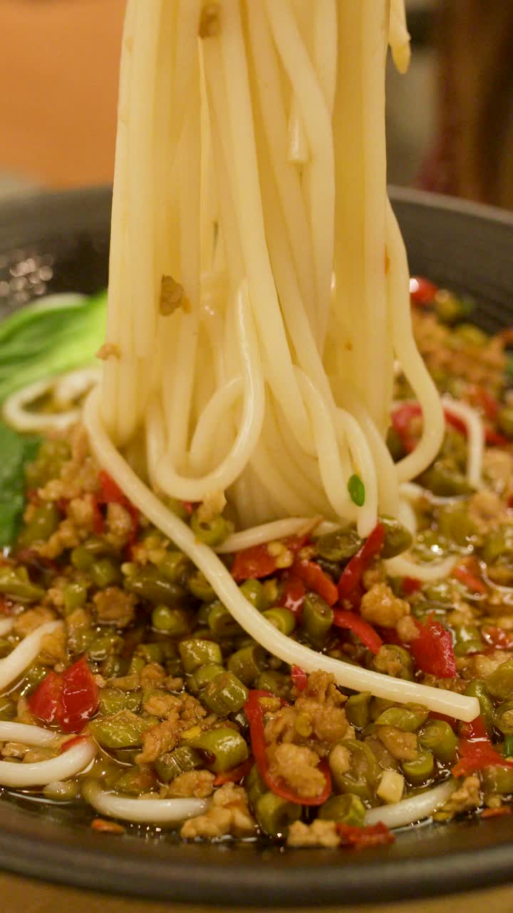 Una mano usa le bacchette per sollevare tagliatelle spesse da una zuppa piccante con verdure e carne macinata