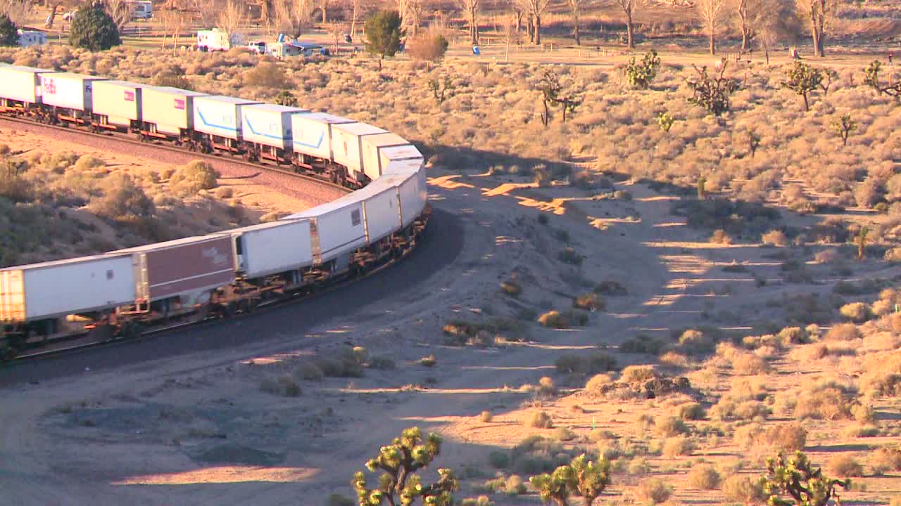 컨테이너 화물열차가 높은 각도에서 사막을 가로질러 이동하고 땅에 그림자를 드리운다
