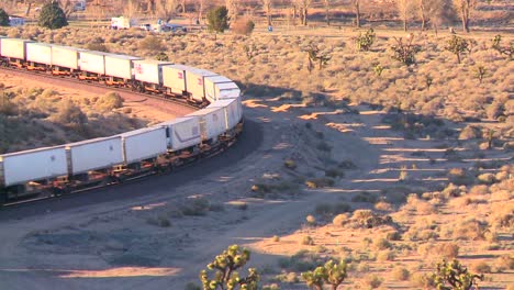 a container freight train moves across the desert from a high angle and casts shadows on the ground