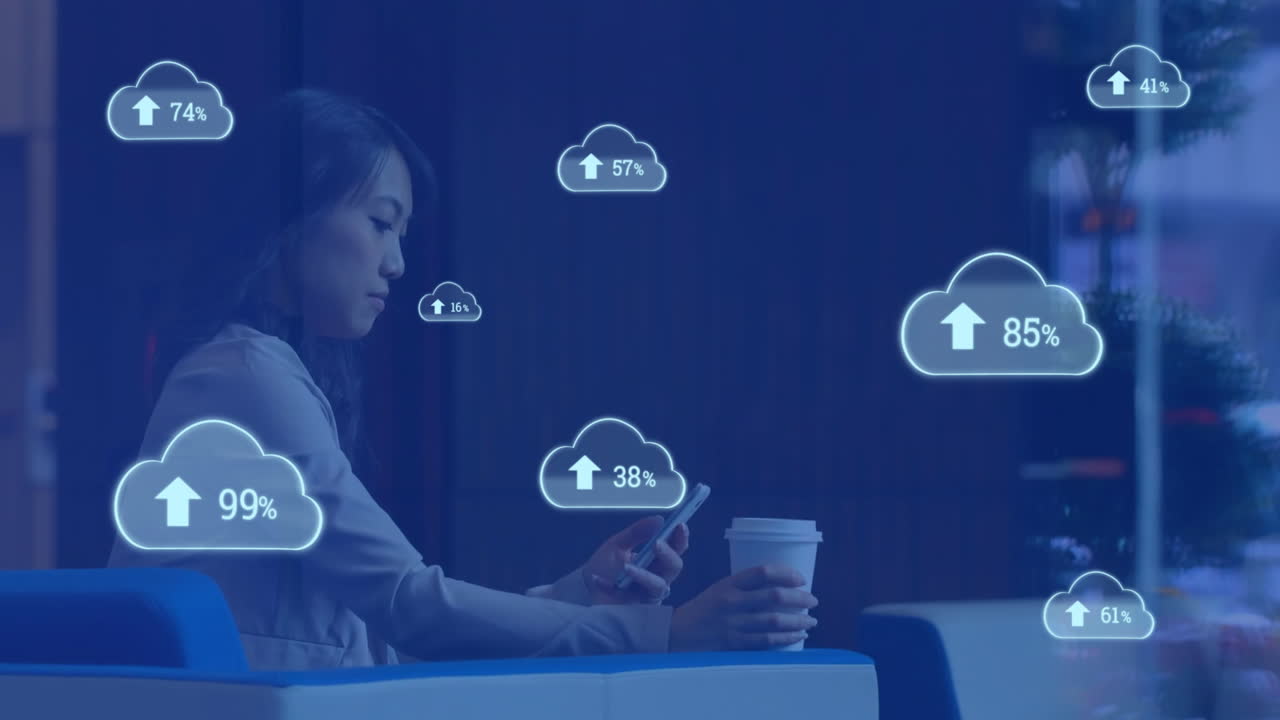 Animation of cloud symbols uploading data over asian businesswoman using smartphone at cafe