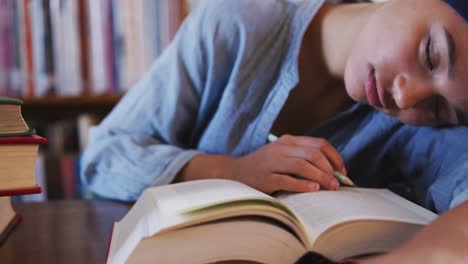 estudiante asiática vestida con un hijab azul sentada en un escritorio con un libro abierto y durmiendo