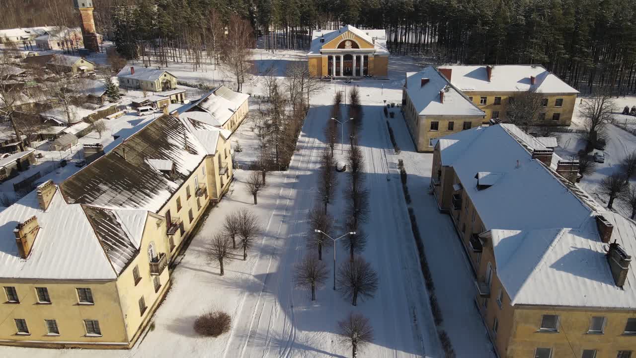 Aerial view of the snow-covered small town of Seda with yellow buildings, streets and roofs covered in white. A peaceful winter landscape in the sunlight.